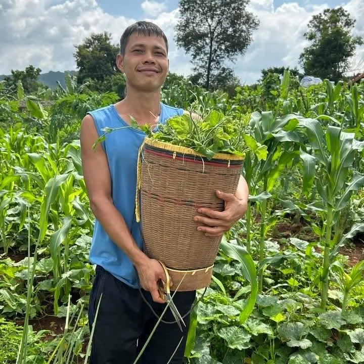 Lê Lam Sơn mặc áo xanh dương, ôm thúng rau giữa khu vườn